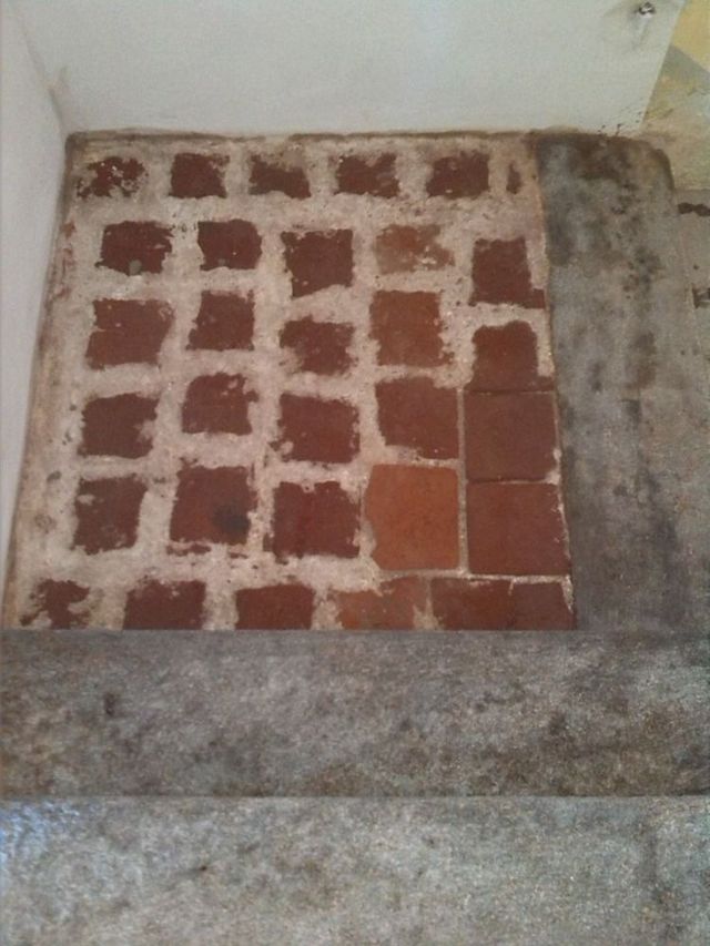Piastrelle quadrate rosse posate su stucco, parte di una sezione del pavimento. Il pavimento confina con gradino grigio.