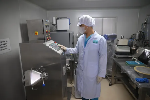 Laboratory workers in blue scrubs and white coats, working with equipment and samples. Bright room with blue floors.