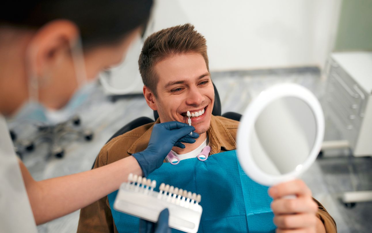 A man is sitting in a dental chair looking at his teeth in a mirror.