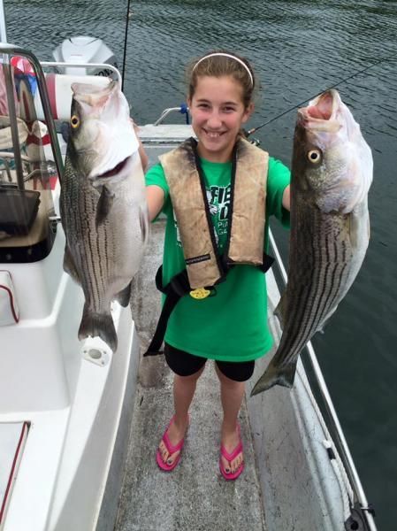 Smiling person on a boat holding two large striped fish over the water