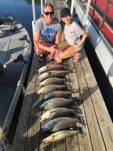 Two people sitting on a dock beside a row of fish laid out on the wooden planks