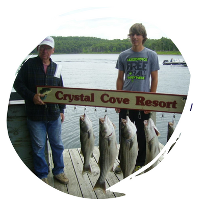 Two people hold a Crystal Cove Resort sign with several fish hanging on a dock by the water.
