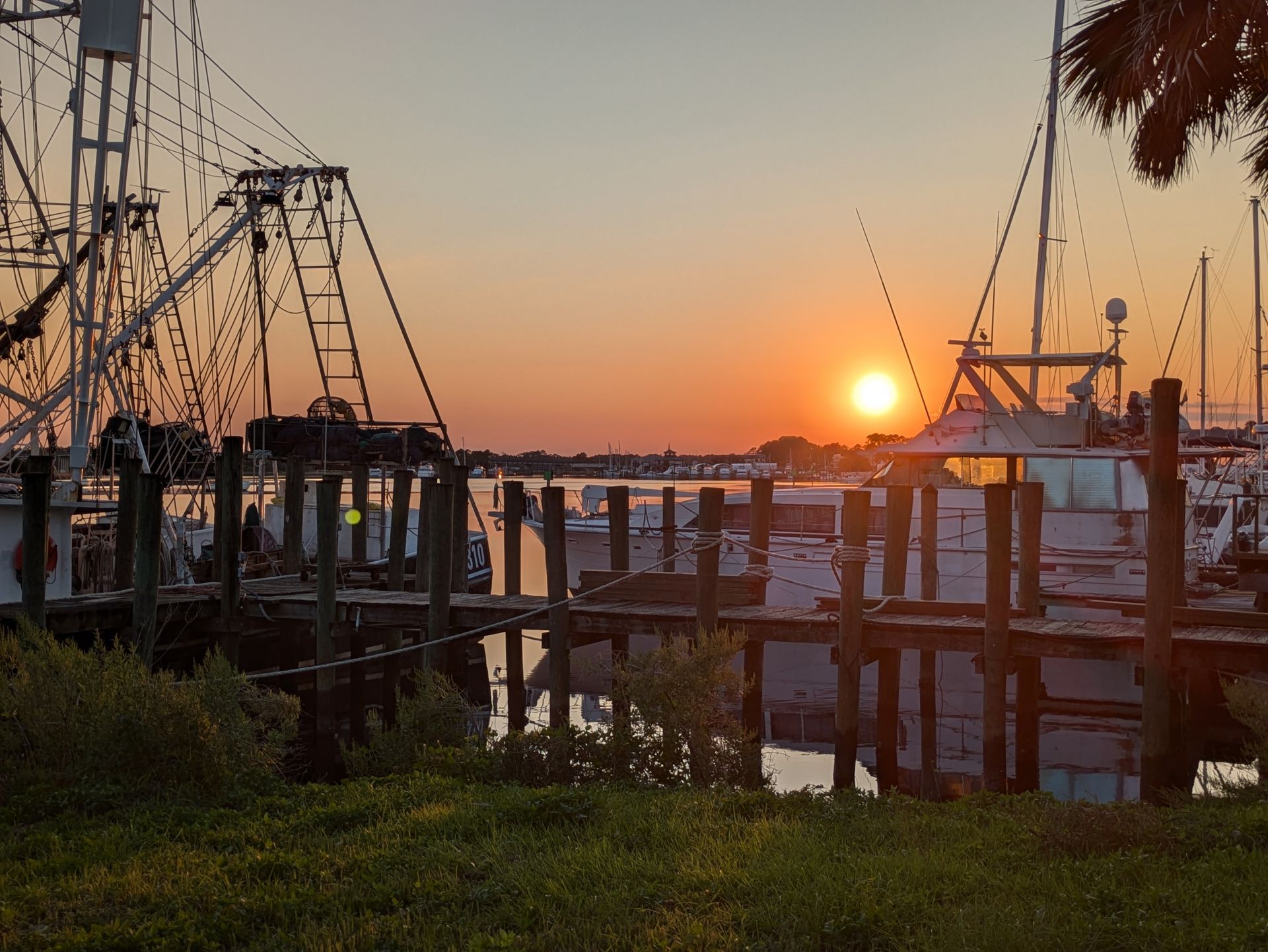 Sunset over a harbor, boats docked along a weathered wooden pier.