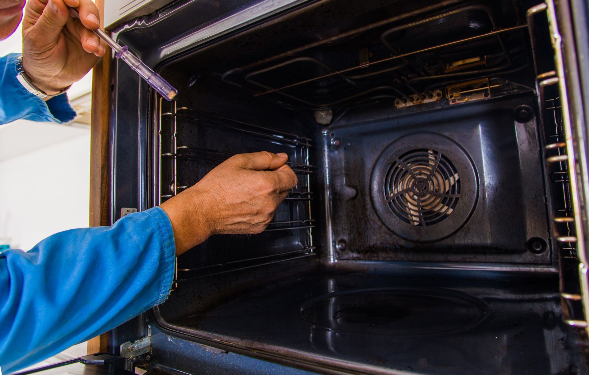 A man is cleaning an oven with a screwdriver.