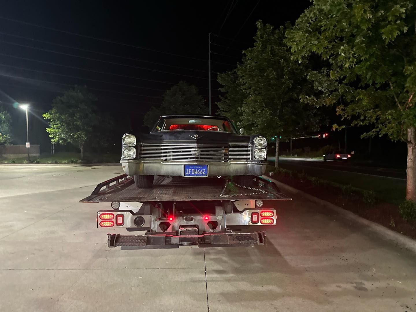 A black classic car is loaded on a flatbed tow truck at night.