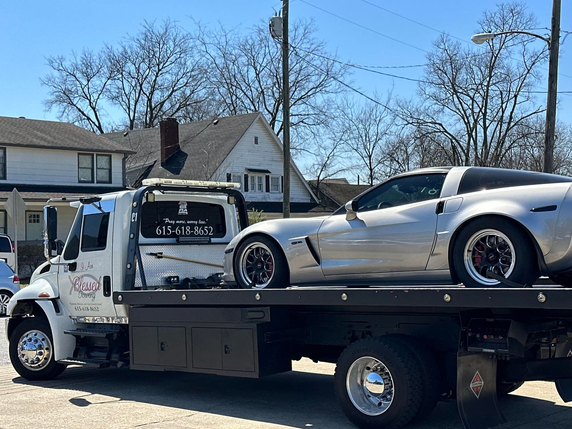 White Corvette on a tow truck in front of a house.