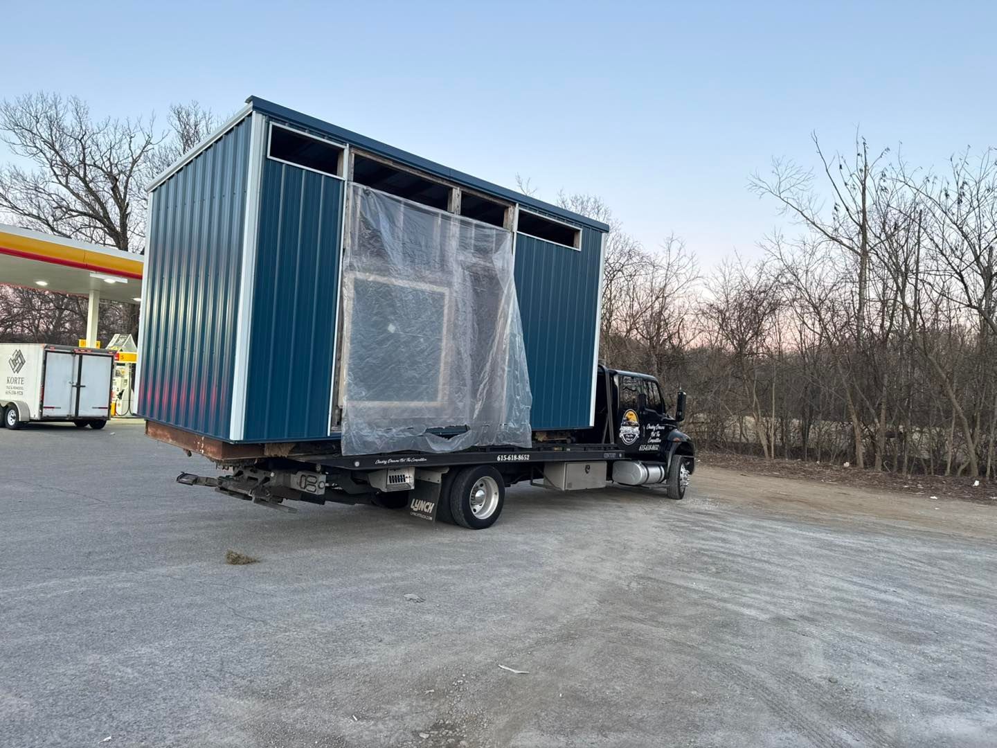 Blue metal building on a flatbed truck at a gas station.