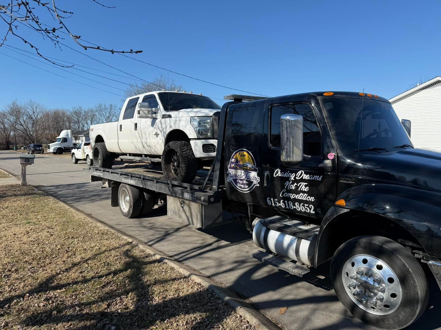 White pickup truck on a black tow truck in a residential area. Clear blue sky.