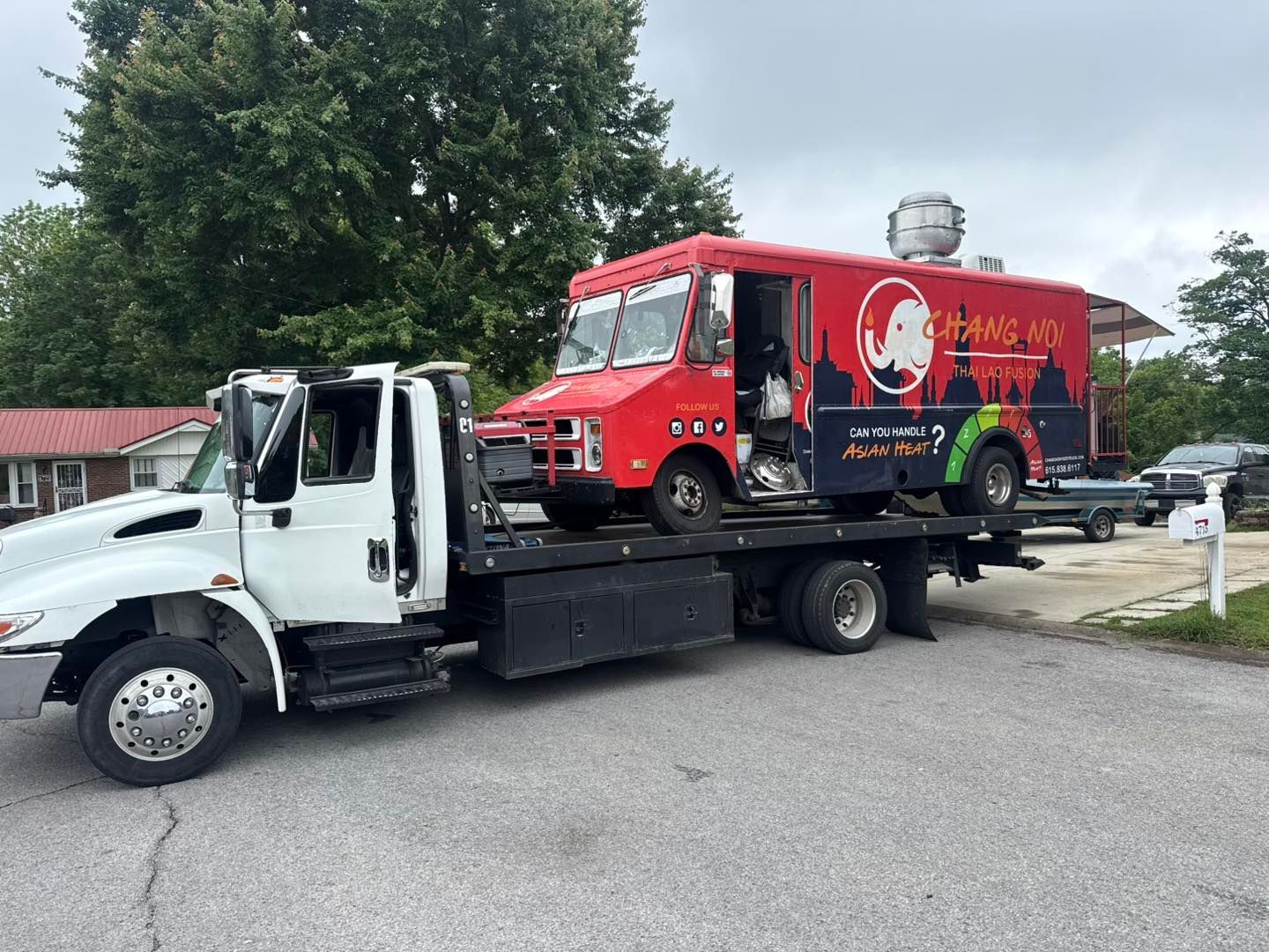 A red food truck being towed by a white tow truck on a paved driveway.
