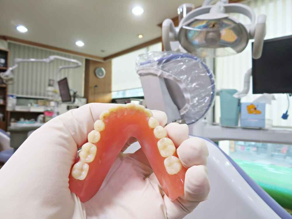 A Person Is Holding A Denture In Their Hand In A Dental Office — Port Denture Clinic In Port Macquarie, NSW