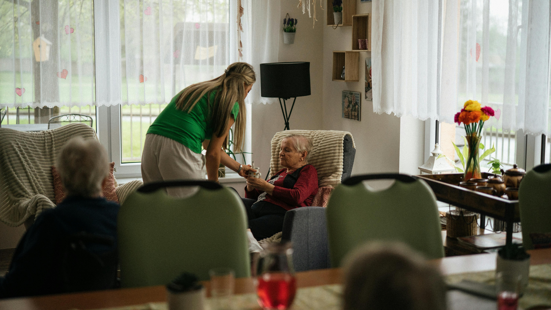 A healthcare provider and an older adult laugh while looking at a tablet together on a couch.
