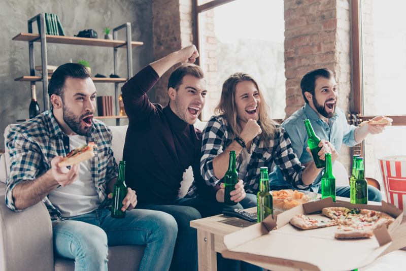 Four men excitedly watching nashville stripper  celebrating with pizza and beer.