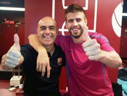 Two men, one with arm around the other, giving thumbs up; in locker room. 