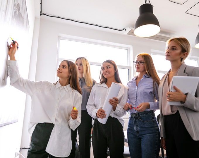 Un equipo de mujeres en un entorno de oficina luminoso, colaborando en una pizarra.
