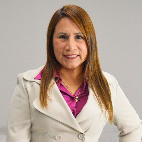 Una mujer con una chaqueta color canela y una blusa rosa sonríe a la cámara, en formato de estudio.