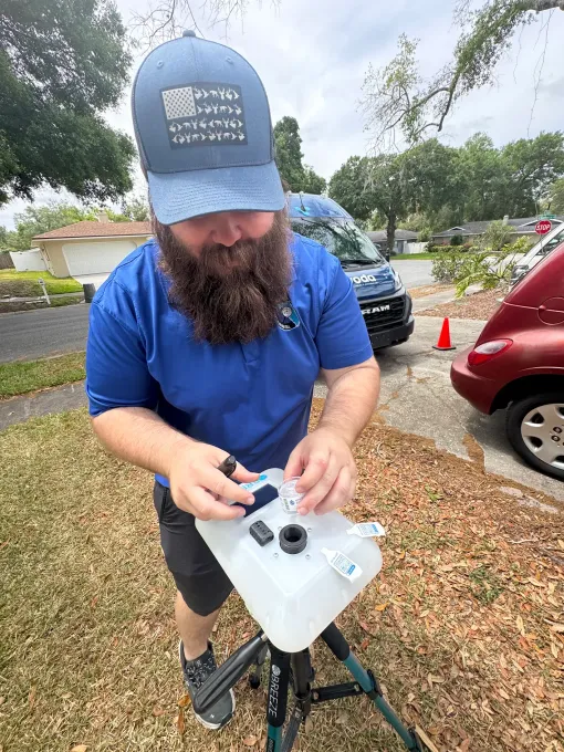 Man in blue shirt operating a drone controller beside parked cars outdoors