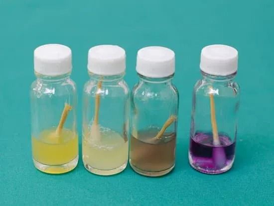Four small bottles with clear liquids and colored solutions on a teal background