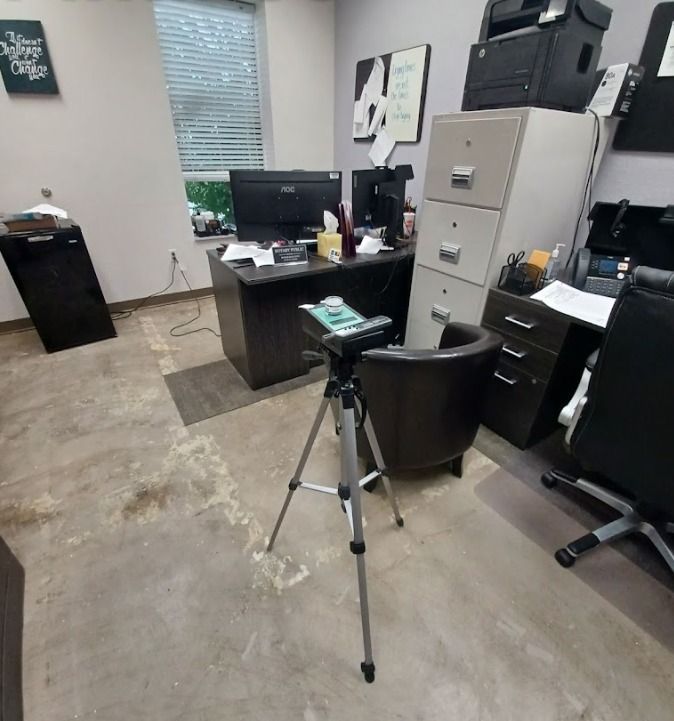 Office with desk, computer, filing cabinet, trash can, and tripod on a concrete floor.
