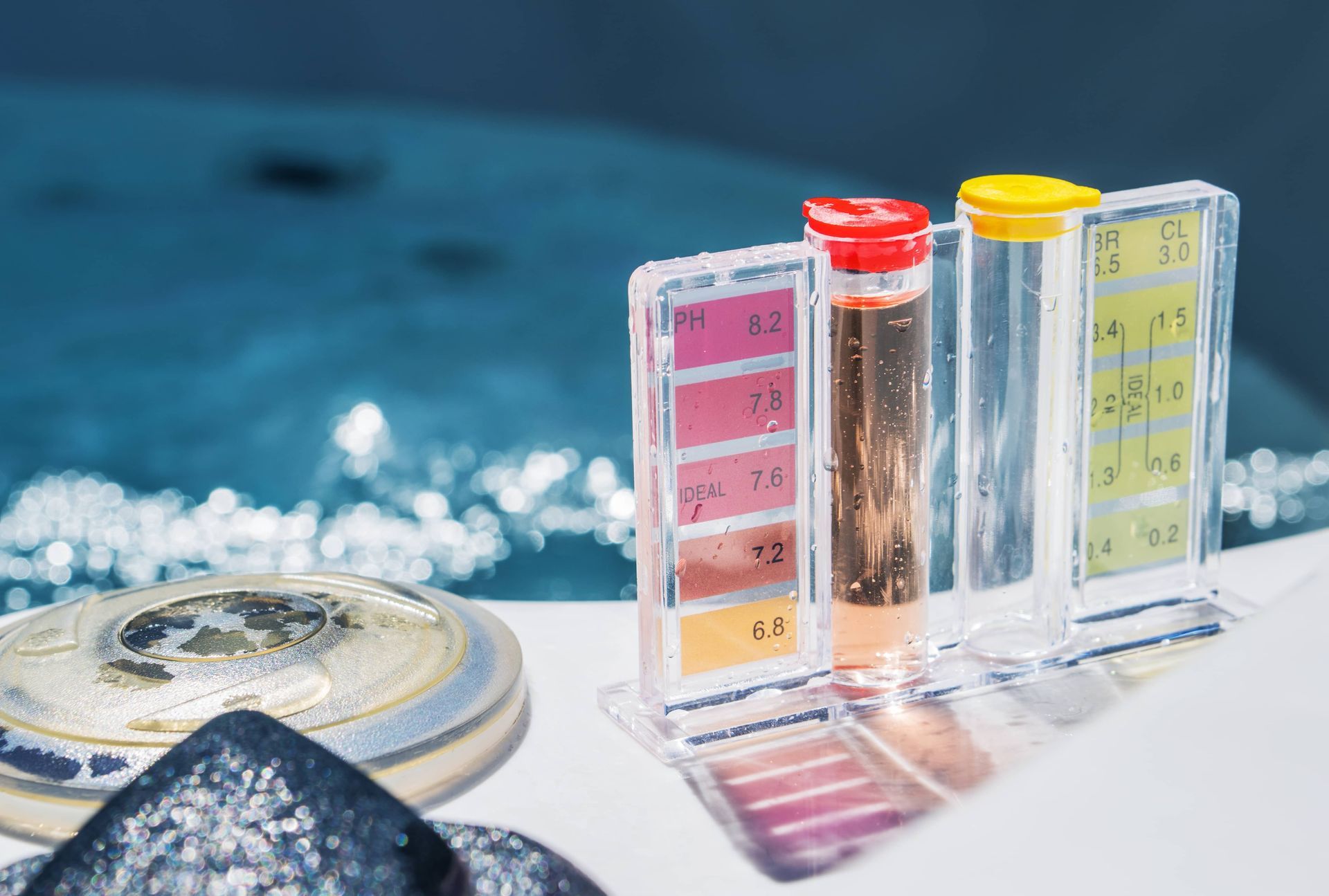 Water quality test strips and vials on a white surface by a pool or spa edge.