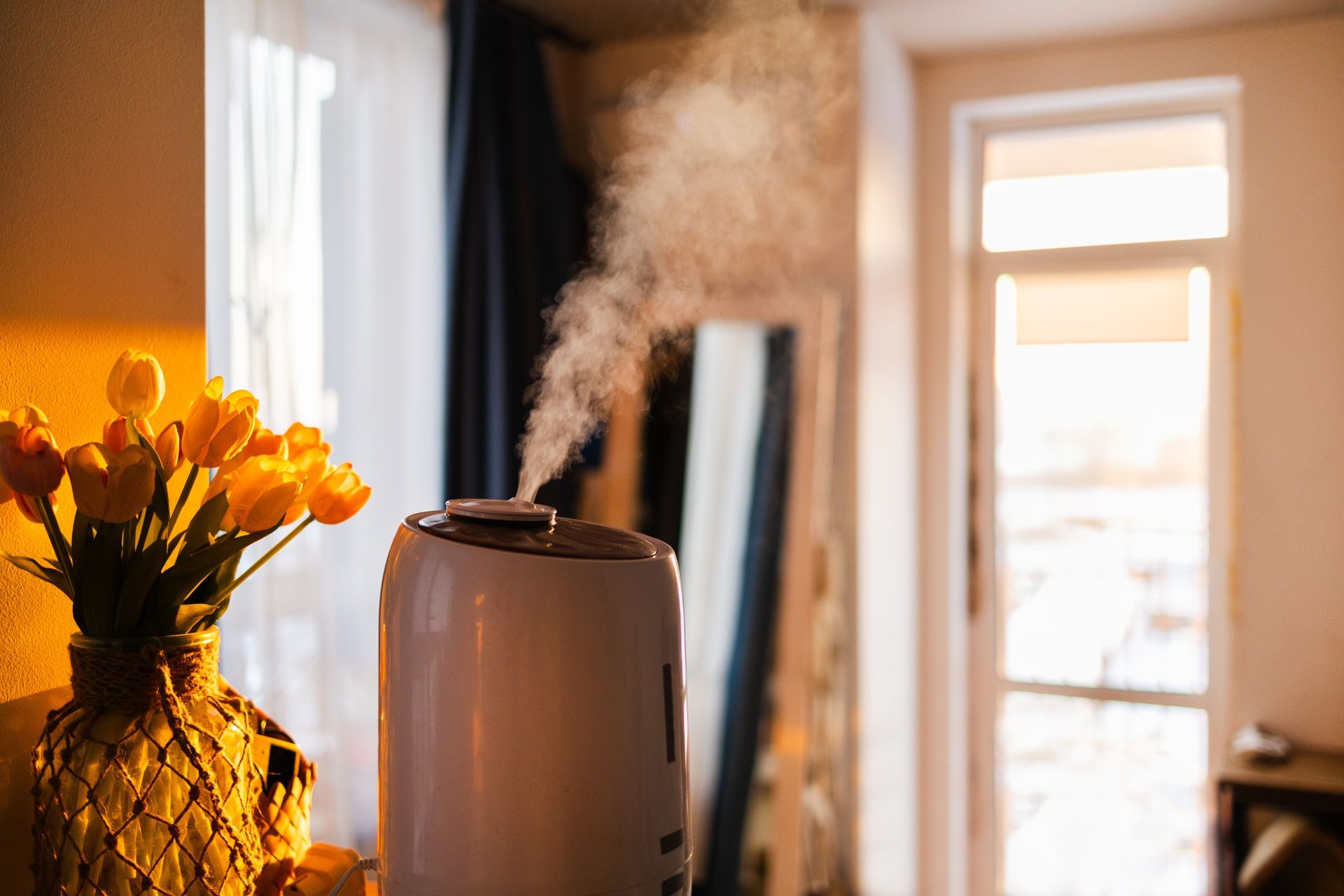 Steaming white humidifier beside yellow tulips near a bright window in a cozy room