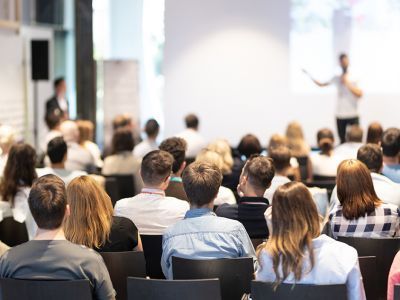 A group of people are sitting in a lecture hall watching a presentation.