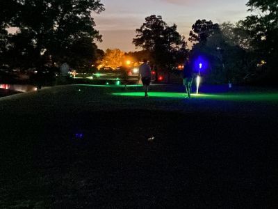 A group of people are walking on a golf course at night