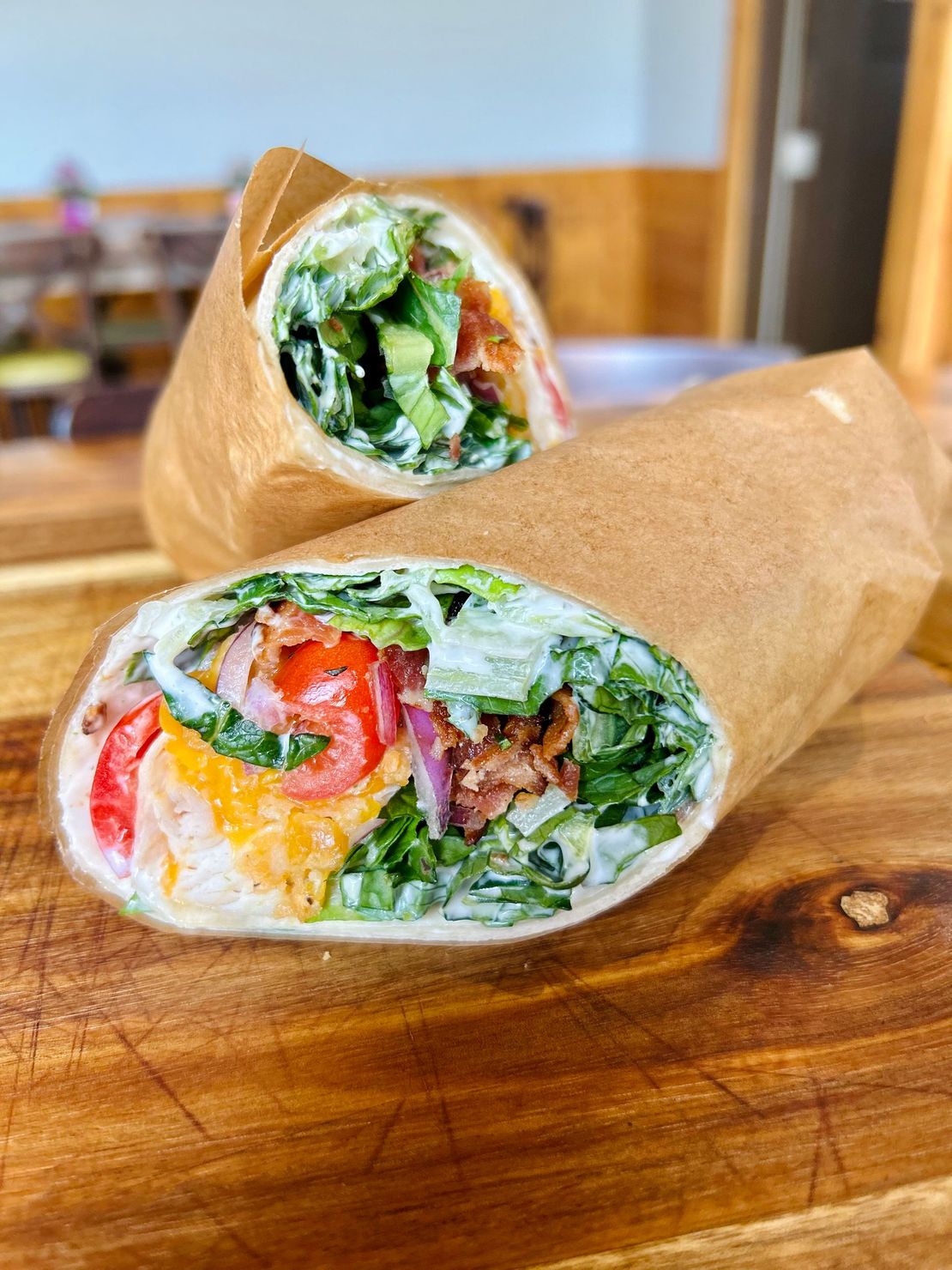 Two chicken Caesar wraps, wrapped in brown paper and served on a wooden board.