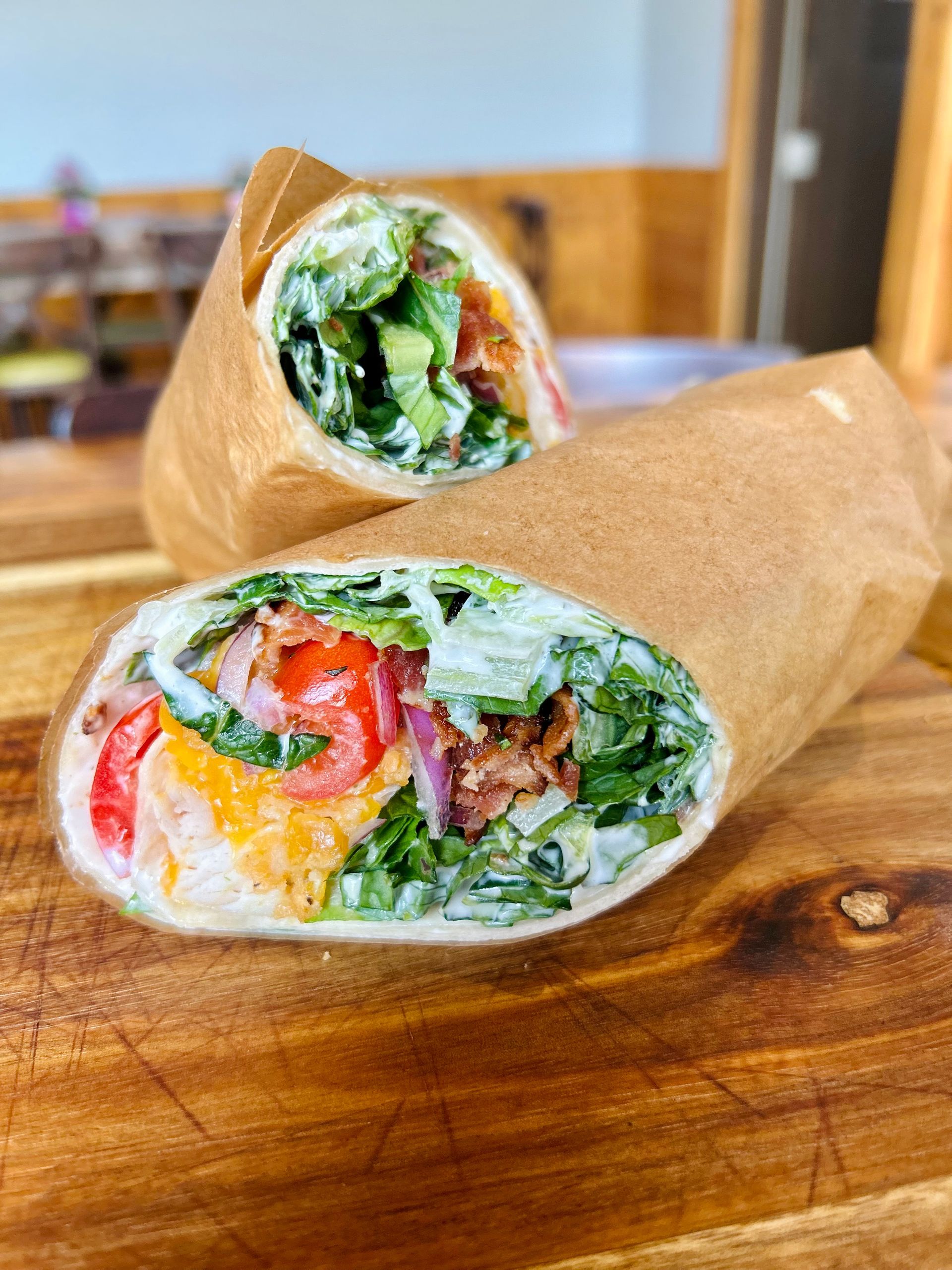 Two chicken Caesar wraps, wrapped in brown paper and served on a wooden board.