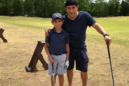 A man and a boy are standing on a golf course holding golf clubs.