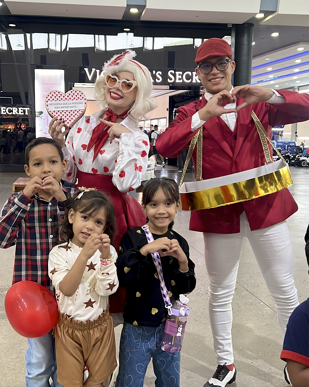Cuatro personas posando en interiores con disfraces festivos, sonriendo y haciendo gestos de corazón con las manos.