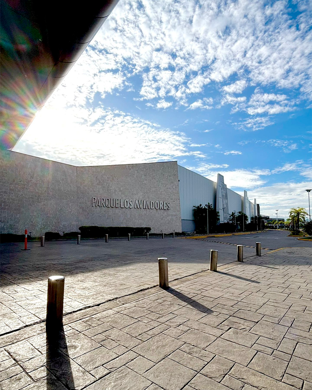 Moderno edificio blanco del museo junto a una plaza de piedra iluminada por el sol bajo un cielo azul con nubes.
