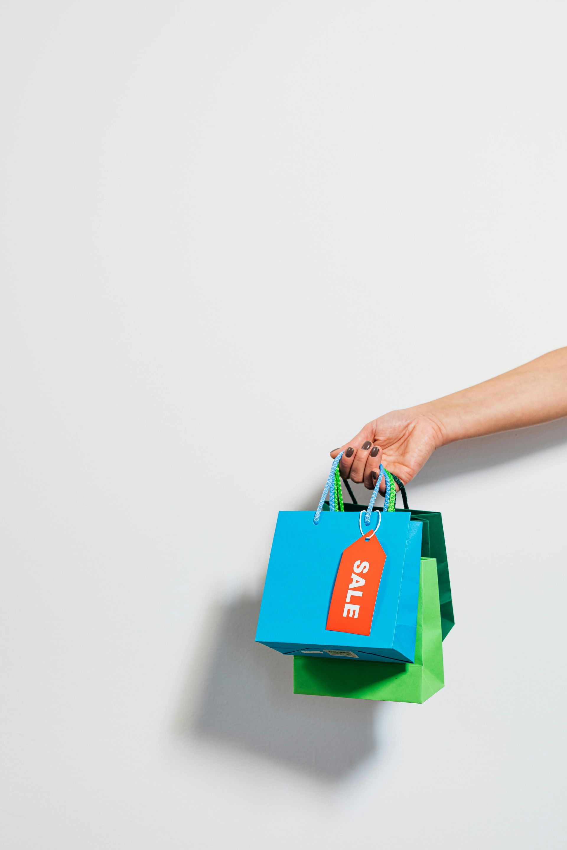 Mano sosteniendo coloridas bolsas de compras con una etiqueta de rebajas sobre un fondo blanco liso.