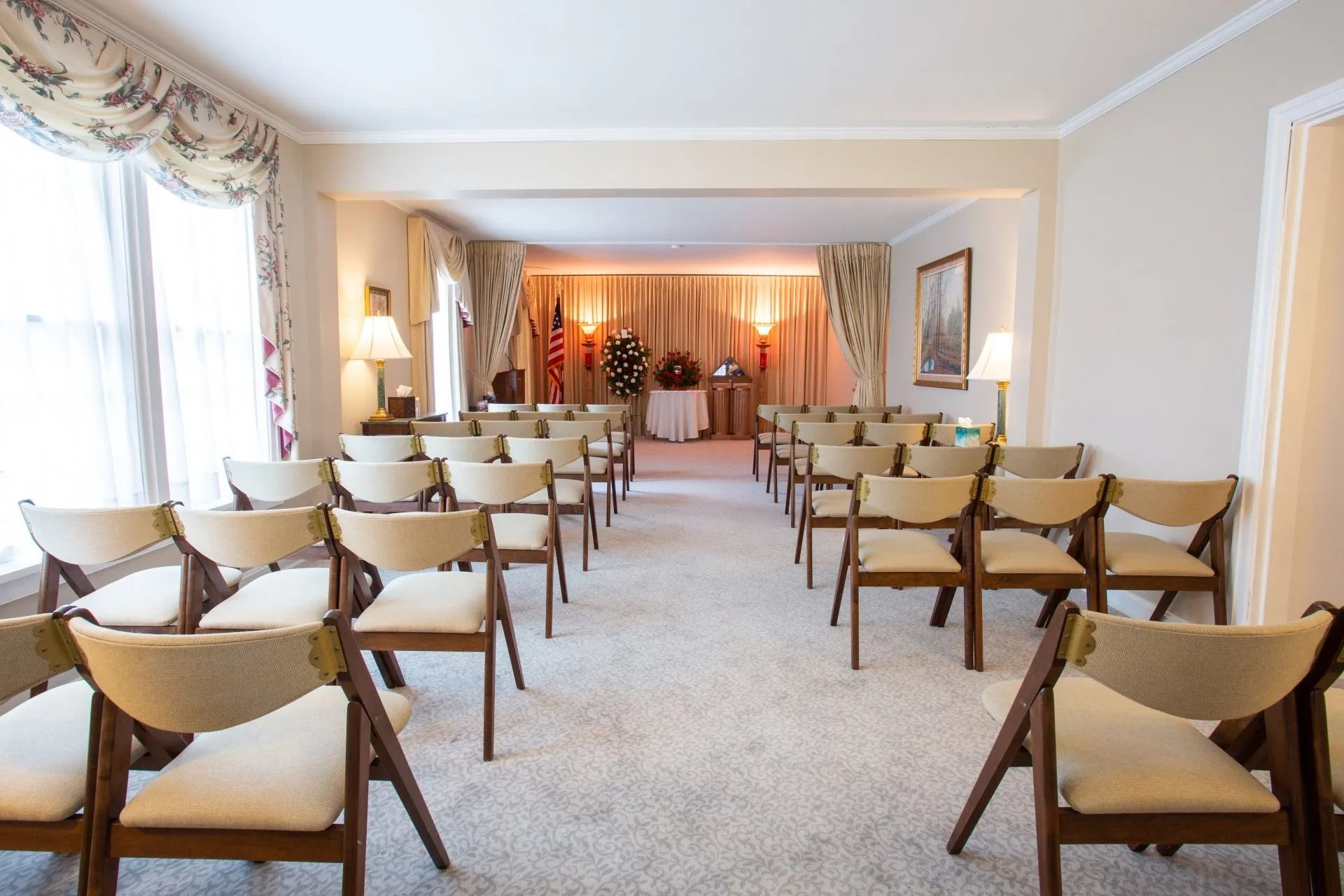 Elegant meeting room with rows of beige chairs facing a small stage with draped curtains.