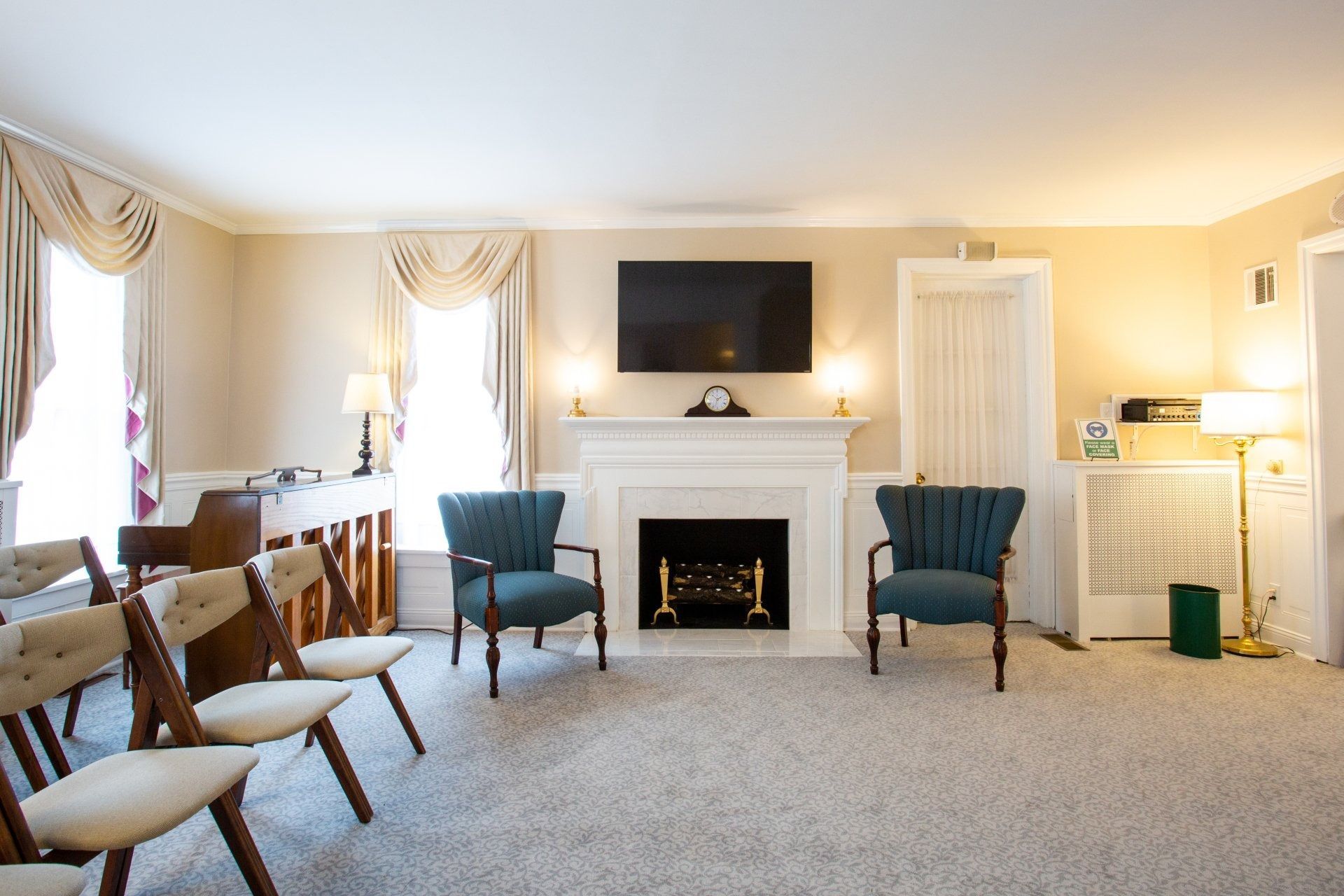 Cozy living room with fireplace, teal chairs, beige carpet, and wall-mounted TV