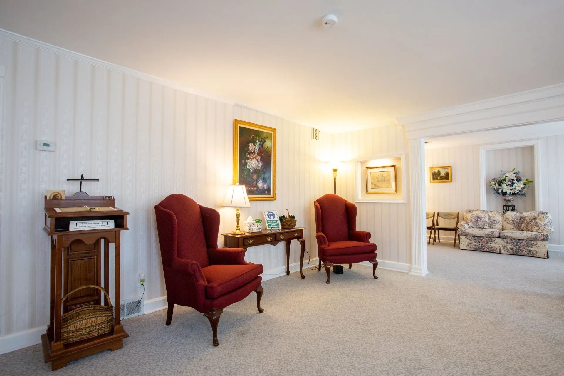 Bright, elegant living room with red armchairs, white walls, and a small wooden fireplace cabinet.