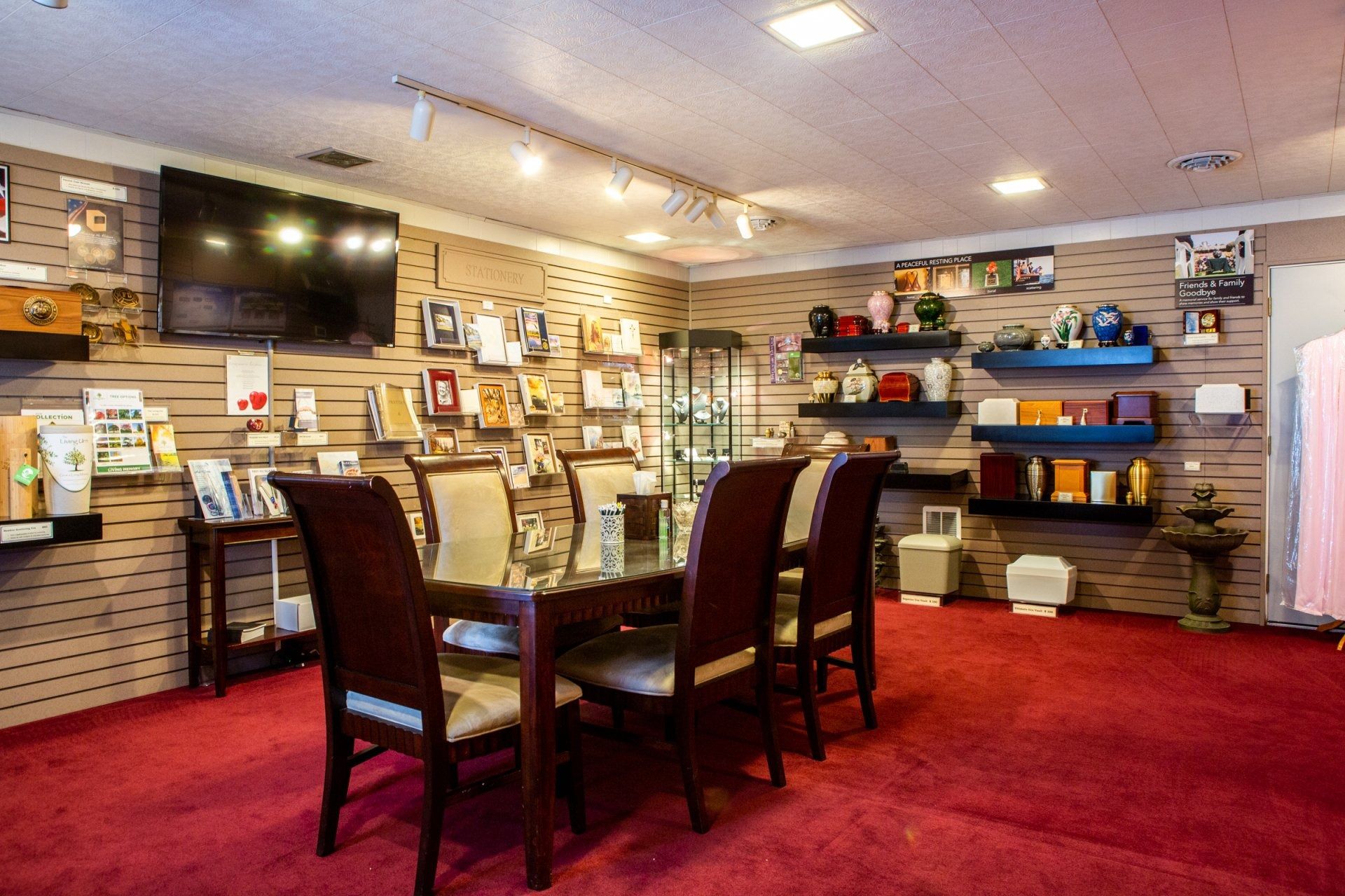 Furniture showroom with red carpet, dining table set, shelves of decor, and wall-mounted TV