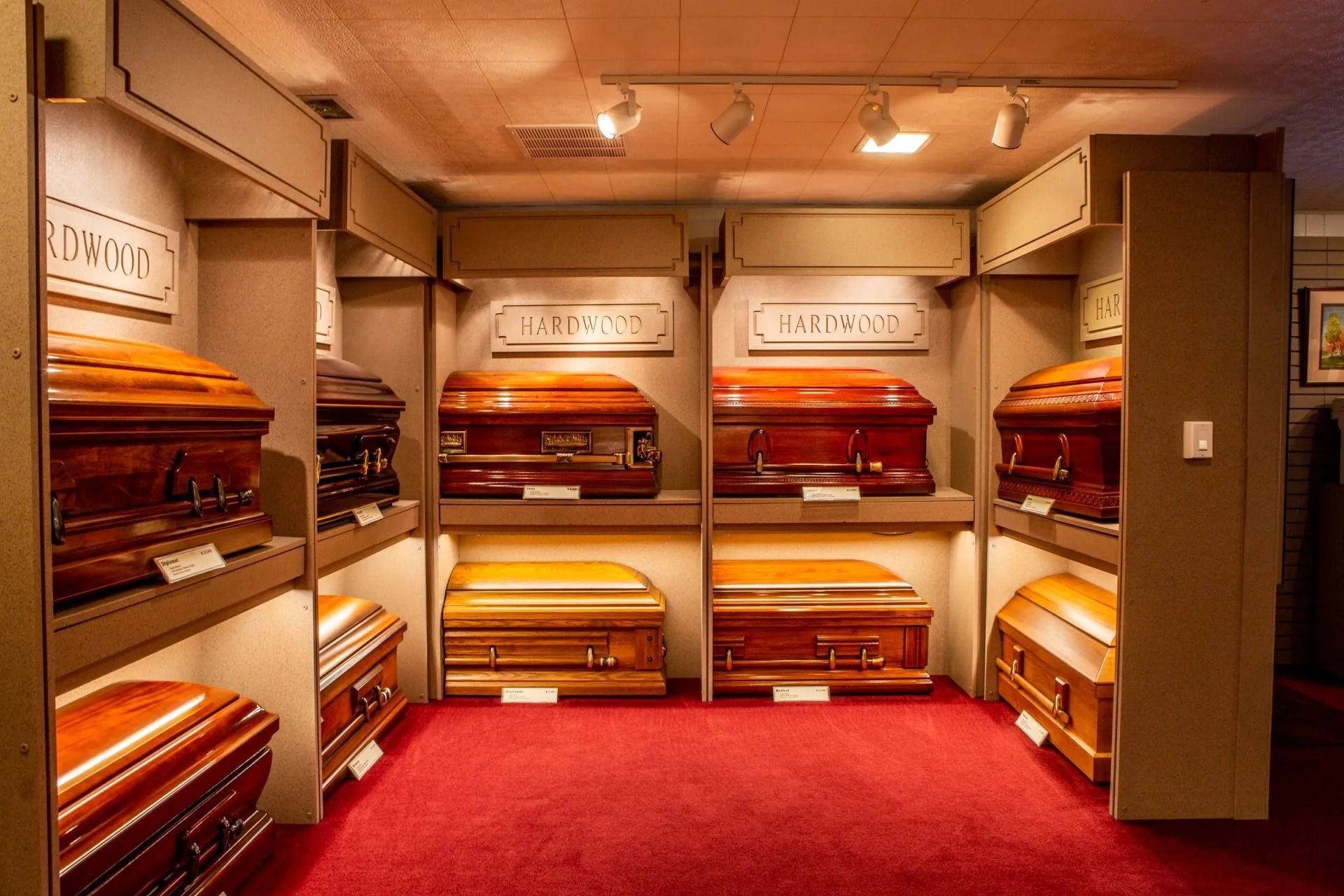 Rows of polished wooden coffins displayed in a red-carpeted funeral showroom.