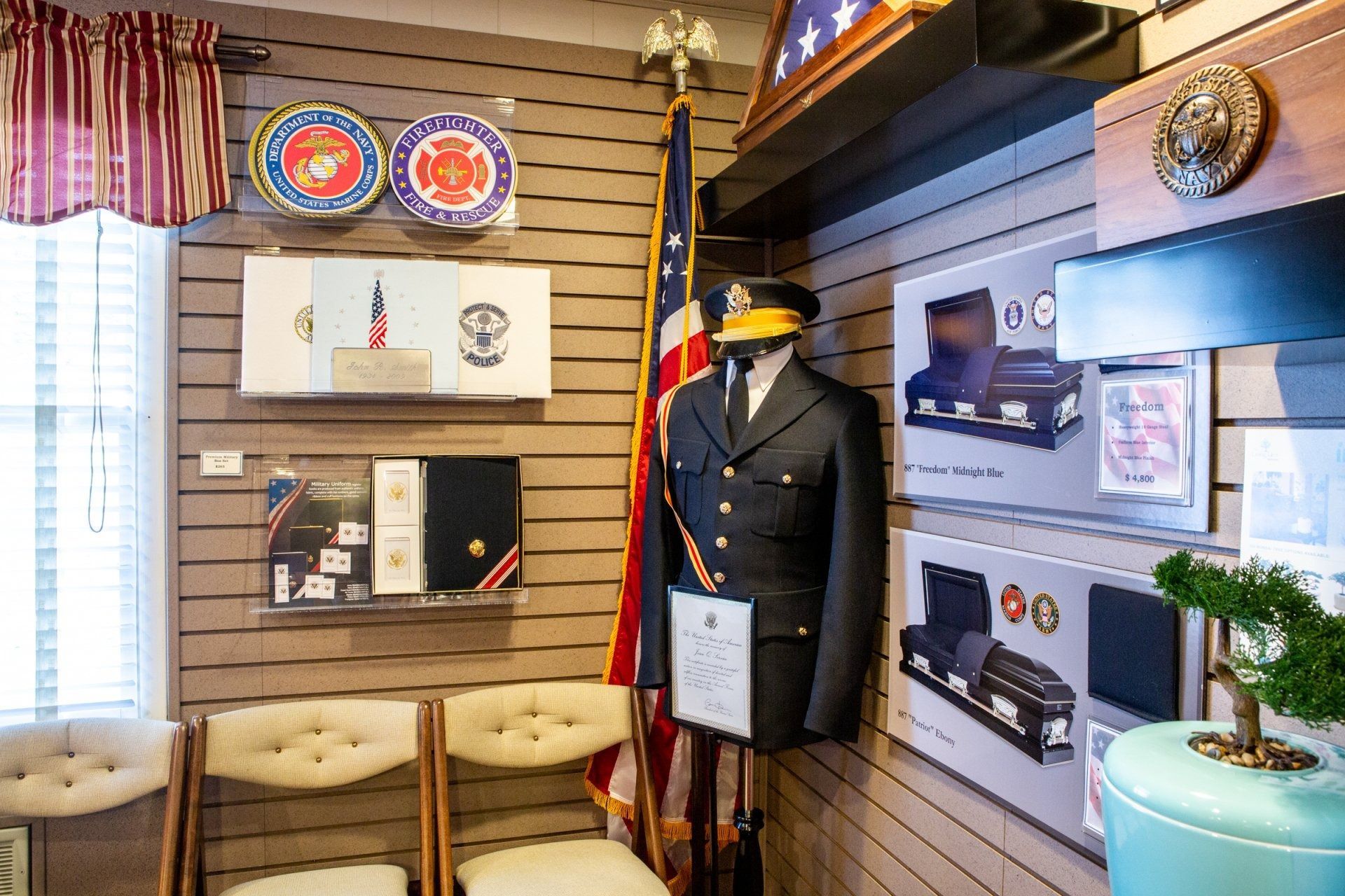Mannequin in a dark uniform inside a small museum exhibit with framed photos and chairs
