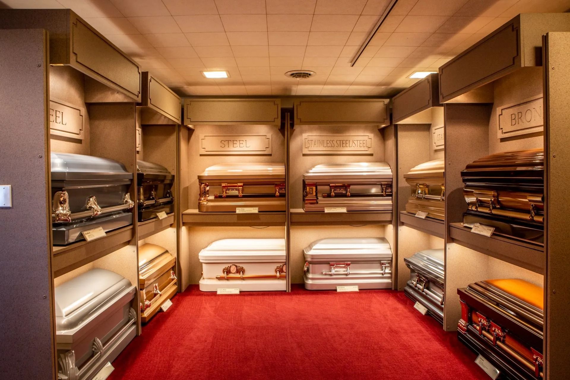 A showroom of open caskets displayed in a red-carpeted room with warm lighting