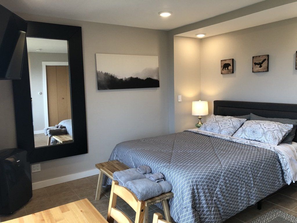 A modern bedroom featuring a bed with gray bedding, a rustic wood bench at the foot, and a large black-framed mirror.