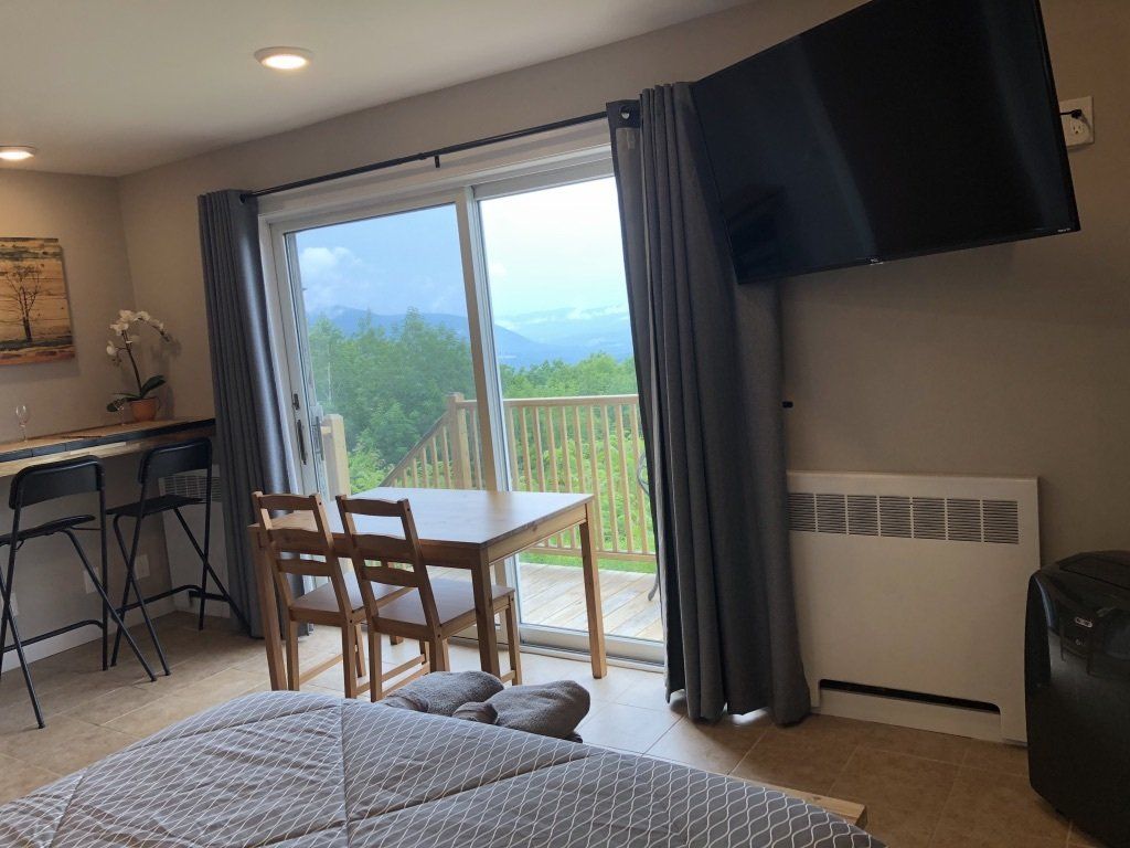 A cozy room featuring a dining table near a sliding glass door with a scenic view, a wall-mounted TV, and a bar area.