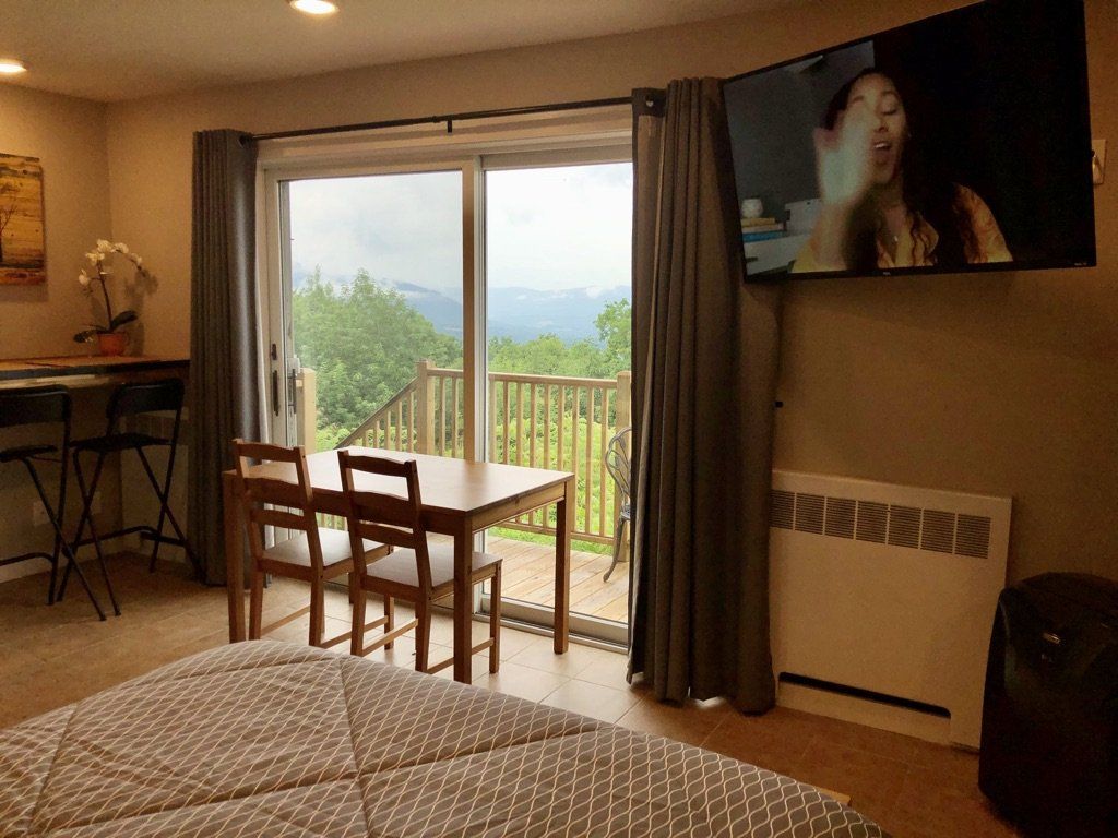 A hotel room with a bed, dining set, and balcony view, featuring a wall-mounted TV playing a video.