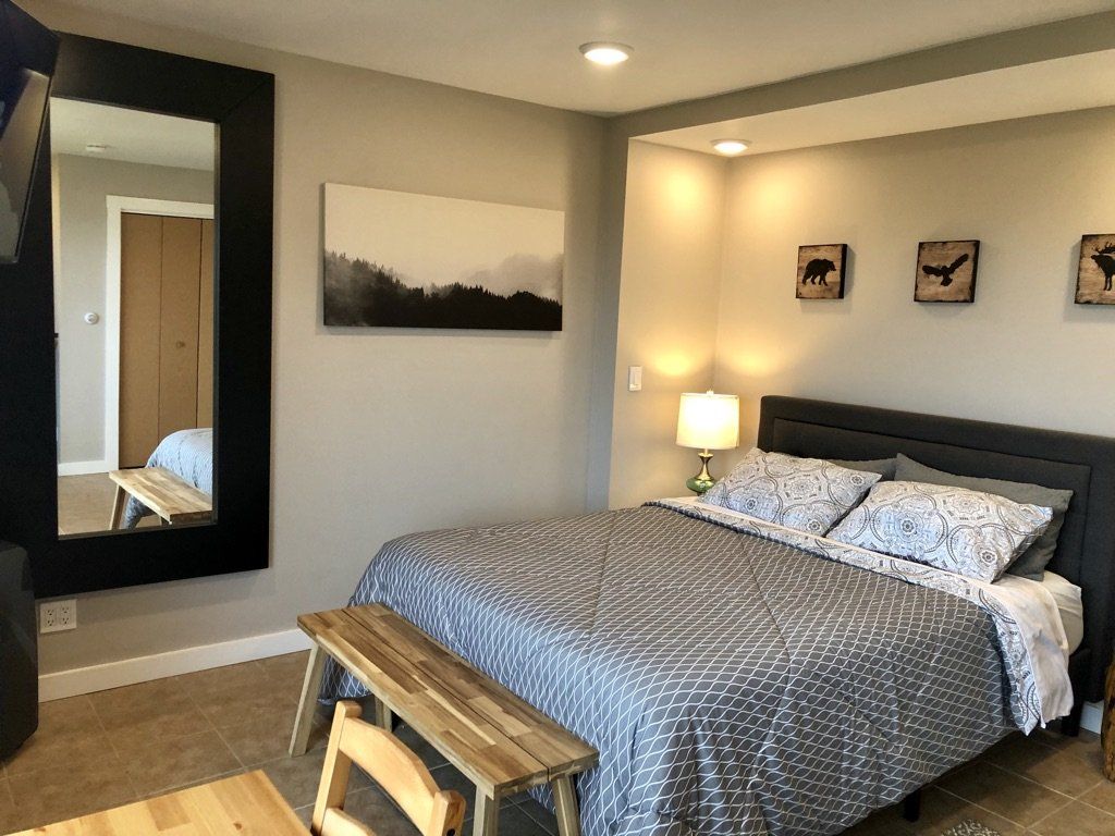 A bedroom featuring a bed with a blue patterned comforter, a wood bench, a mirror, and wall art.