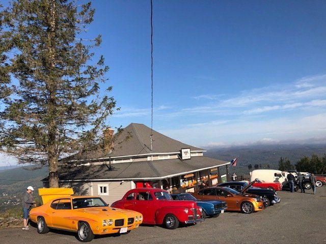 Classic cars parked outside a mountainside building on a sunny day.