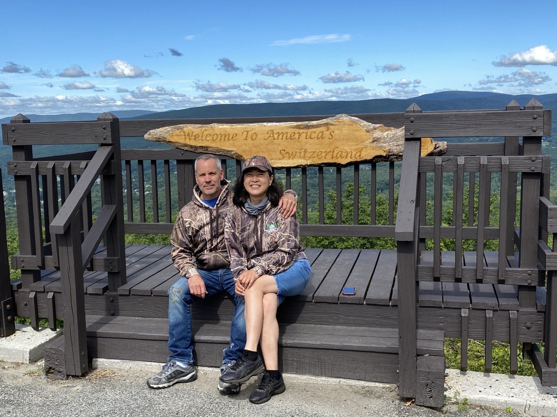 A couple sitting on a wooden bench at an overlook with a sign reading 