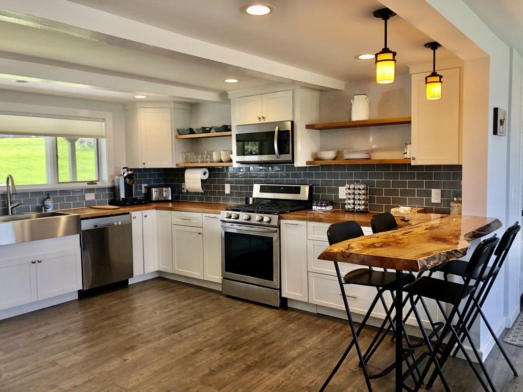 Modern kitchen with white cabinetry, stainless steel appliances, grey subway tile backsplash, and a live-edge wood island.