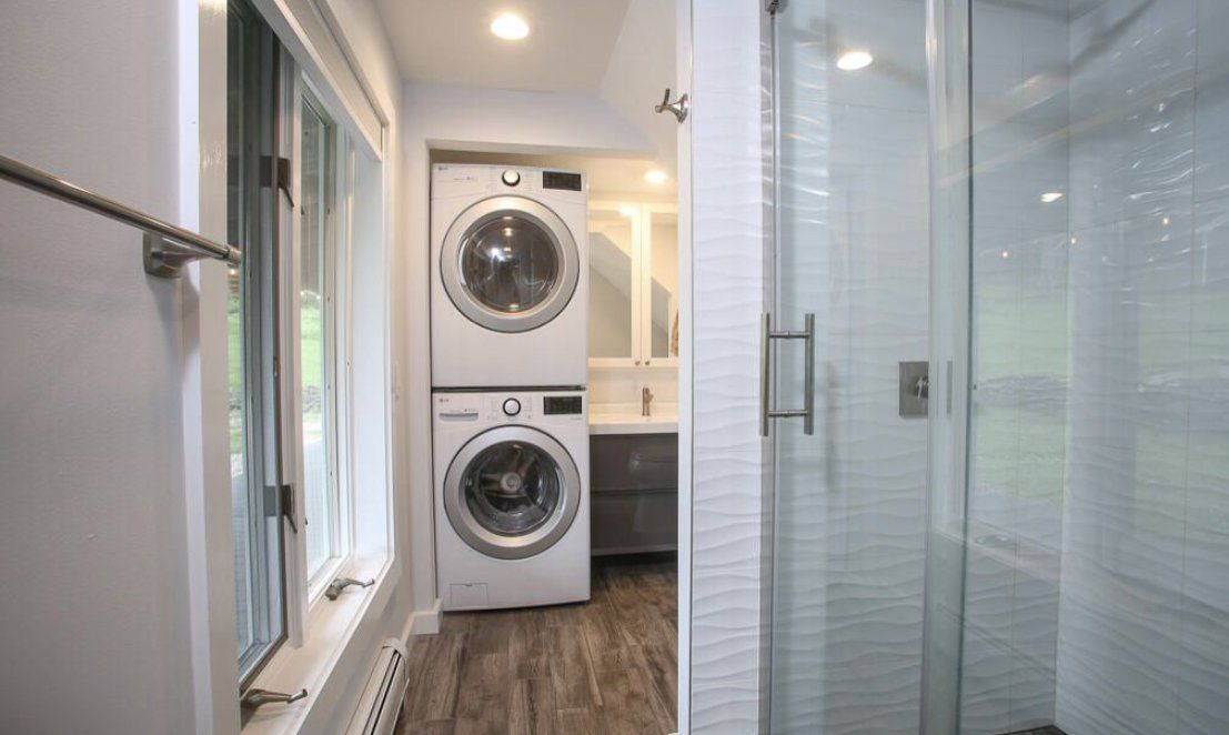 A compact bathroom featuring a stacked washer and dryer unit, a glass shower stall, and a small vanity area.