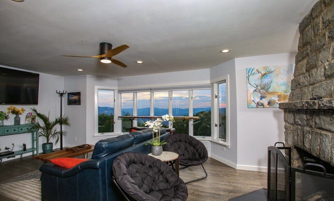 A cozy living room with a stone fireplace, blue sofa, and large windows offering a scenic mountain view.