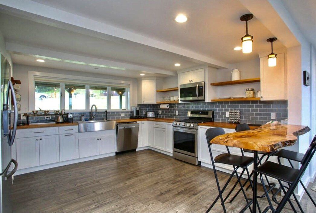 A modern kitchen featuring white cabinets, wood countertops, a stainless steel sink, and a live-edge wooden dining table.