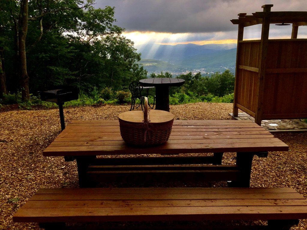 Picnic table with a basket in a park overlooking mountains and a valley during a cloudy sunset.